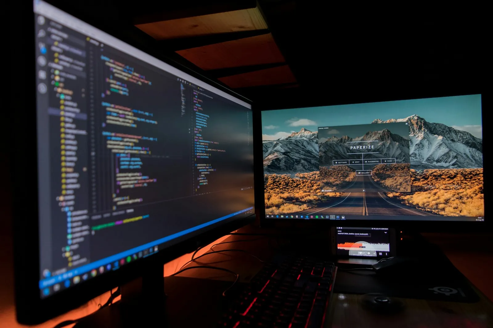 Zwei Monitore im abgedunkelten Raum: links farbiger Code im Editor, rechts ein Bergpanorama mit dem Fenster "Paperize"