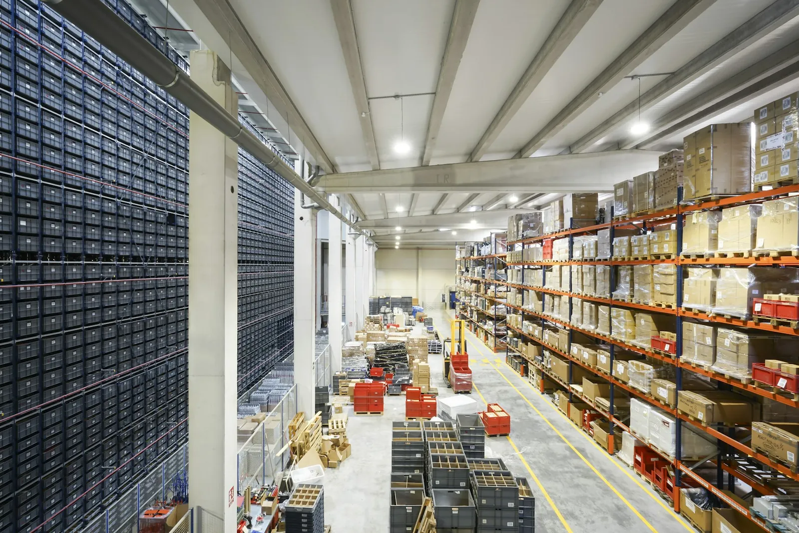 Blick von oben in eine Lagerhalle mit hohem Behälterlager links und orangefarbenen Palettenregalen rechts