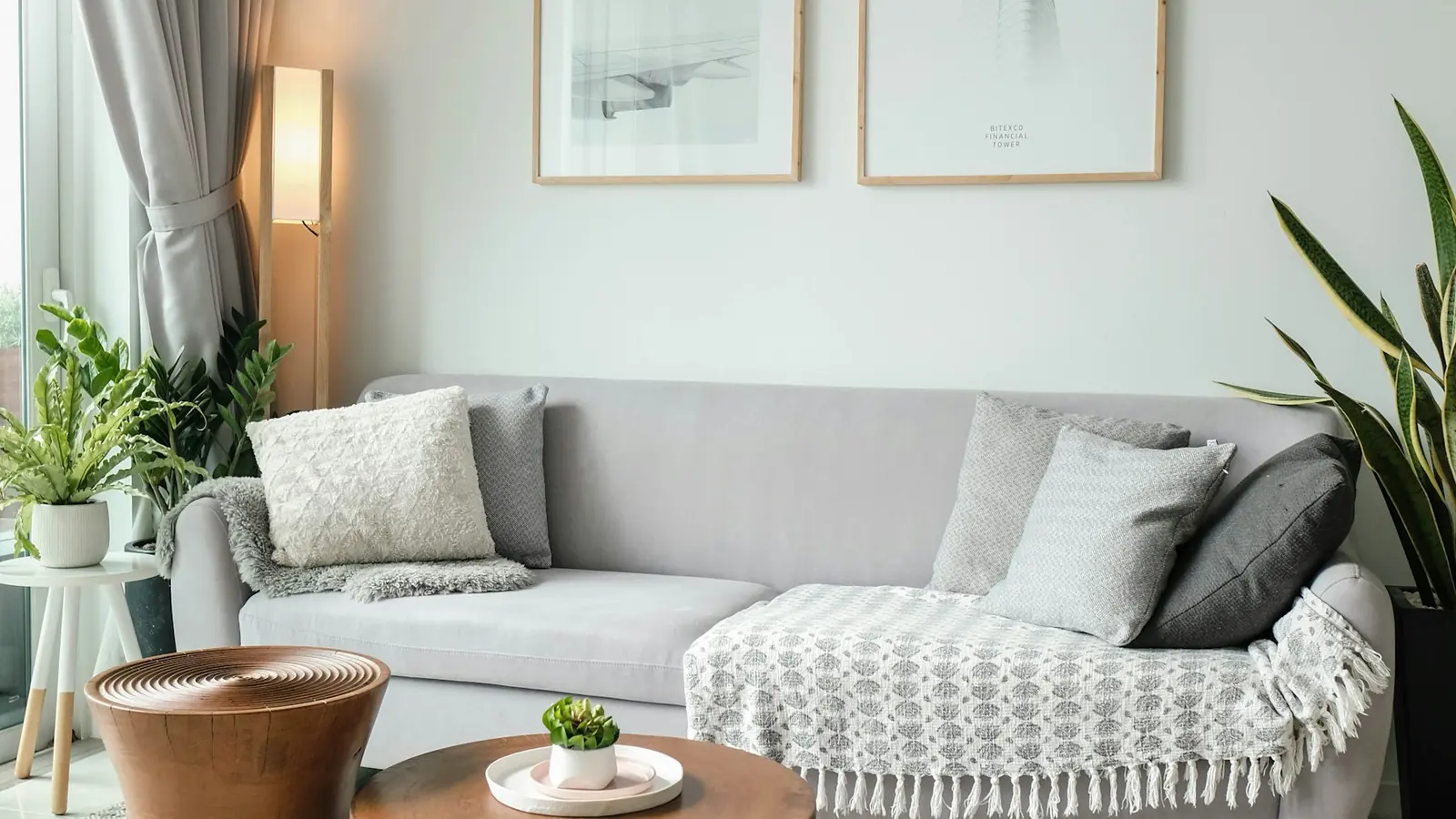 Helles Wohnzimmer mit grauem Sofa, runden Holztischen, Strickpouf und zwei gerahmten Drucken, einer mit „Bitexco Financial Tower"