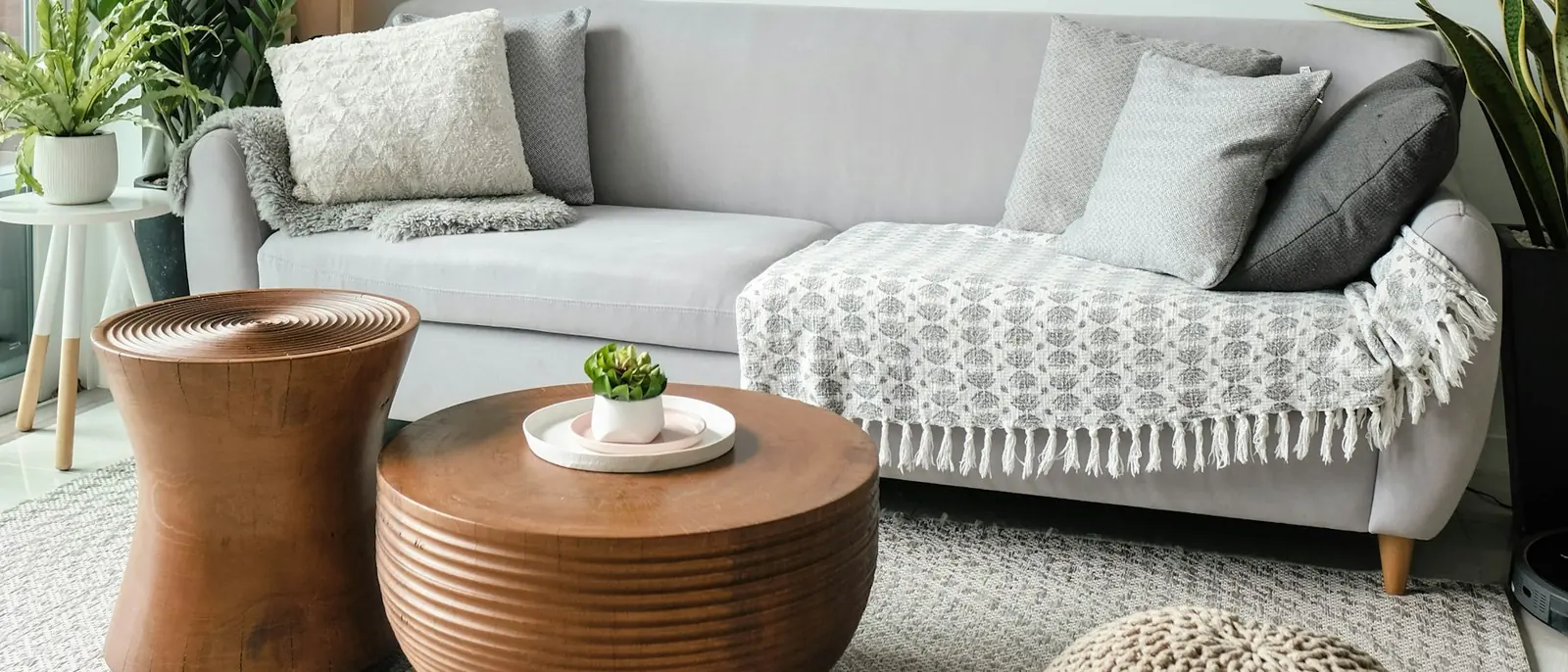 Helles Wohnzimmer mit grauem Sofa, Kissen und Pflanzen